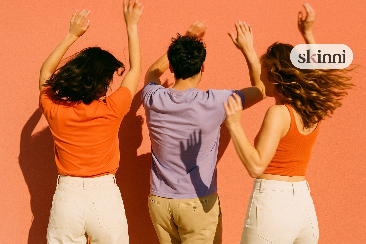 Three friends dancing against a bright coral wall, photographed from behind